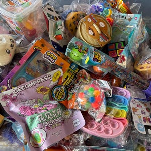 May include: A collection of colorful sensory toys and games, including squishy toys, pop-its, and Goo Games. The image features various packaged items with text like "DECOMPRESS" and "SENSORY TOY".