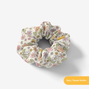 May include: A white scrunchie with a floral pattern featuring pink, yellow, and blue flowers. The scrunchie is made of soft, stretchy fabric and is perfect for holding hair in place.