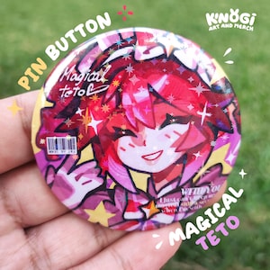 Può includere: Un bottone a spillo rotondo con un'illustrazione colorata in stile anime. Il design presenta un personaggio con i capelli rossi e il testo "MAGICAL TETO" e "PIN BUTTON". La spilla ha un effetto olografico lucido ed è tenuta in mano.