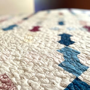 Op de afbeelding: Een wit quilt met een patchwork ontwerp met blauwe, rode en witte stof. Het quilt is gestikt met een golvend patroon.
