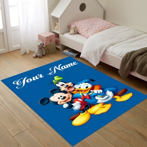May include: A blue rug with the text 'Your Name' in white. The rug features a cartoon image of Mickey Mouse, Donald Duck, and Goofy. The characters are smiling and standing together. Mickey Mouse is wearing red shorts and yellow shoes. Donald Duck is wearing a blue sailor shirt and red bow tie. Goofy is wearing a green hat and brown pants.