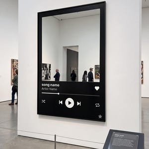 Może przedstawiać: Czarna lustro w ramie z interfejsem odtwarzacza muzyki. Interfejs wyświetla "song name" i "Artist Name" z ikonami odtwarzania, pomijania i polubienia. Lustro odbija wnętrze muzeum z dziełami sztuki i zwiedzającymi.