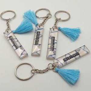 May include: Keyrings with rectangular pendants displaying the word "ERROR" in black. The pendants have a white and blue design, attached to silver keyrings with blue tassels.