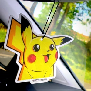 May include: Yellow cartoon character car air freshener with a black outline and the text "ANIFRESH" at the bottom. The character has a large smile and a red tongue sticking out.