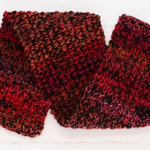 Puede incluir: Una bufanda de punto roja, negra y naranja con un patrón texturizado.