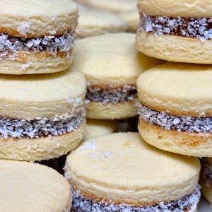 May include: A stack of shortbread cookies with dulce de leche filling and a sprinkle of coconut flakes. The cookies are light brown and the filling is a rich brown color.
