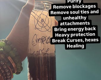 May include: A clear glass candle container filled with a two-toned substance, featuring a light-coloured top layer and a dark-coloured bottom layer. The glass is marked with handwritten text reading D Restore Me, Cleanse, and Cleanse.