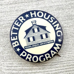May include: A vintage pin with a blue and white design. The pin features the text "BETTER HOUSING PROGRAM" around the edge, with a house illustration in the center. The words "FEDERAL HOUSING ADMINISTRATION" are at the bottom.