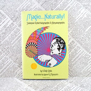 May include: A yellow book titled Magic...Naturally! Science Entertainments & Amusements by Vicki Cobb, illustrated by Lance R. Miyamoto. The cover features a black and white illustration of a person holding a wand against a bright blue and pink sunburst.