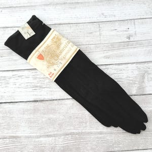May include: A pair of black gloves with a label wrapped around the wrist. The label reads "Chamoisuede Washable Gloves" and includes the size "6 1/2". The gloves are made of a soft, dark material.