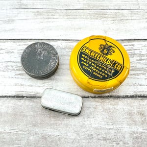 May include: Three vintage metal tins of varying shapes and sizes. A round, dark gray tin with embossed text, a yellow tin with the text "SMARTCHILD & CO.", and a small rectangular tin with text.