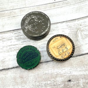 May include: Three vintage metal tins with text. One is dark gray with faded text, another is green with "BENJ. ALLEN & CO Watch Materials and Tools" and the third has a paper label with handwritten numbers.