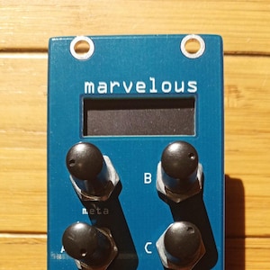 May include: A blue modular synthesizer panel featuring the text marvelous, meta, B, C, CV1, CV2, CV3, CV4, CV5, CV6, left, right, and poetaster's tonetoys. The device includes four black rotary knobs, eight metal input jacks, and two small white illustrations.