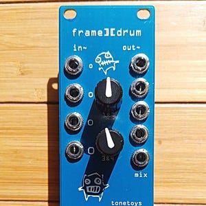 Può includere: Un modulo Eurorack blu e bianco con il testo "frame][drum" e "tonetoys poetaster's" stampato su di esso. Il modulo ha due manopole, quattro jack e quattro interruttori a levetta.