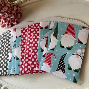 May include: A collection of small gift bags with various patterns. Designs include black polka dots, red polka dots, and a light blue pattern with gnome illustrations. The bags have a scalloped edge.