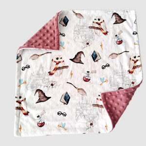 Può includere: Una coperta per bambini bianca con un bordo a pois minky rosa. La coperta presenta un motivo ripetuto di gufi, cappelli da mago, libri, scope, occhiali e fulmini. La coperta misura circa 76 cm per 102 cm.