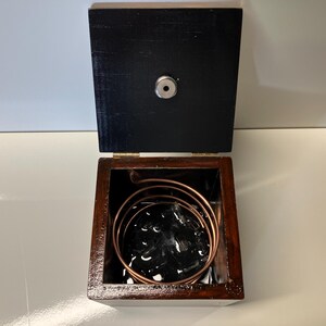 May include: A wooden box with a black interior and a copper coil inside. The box is open and the coil is visible.