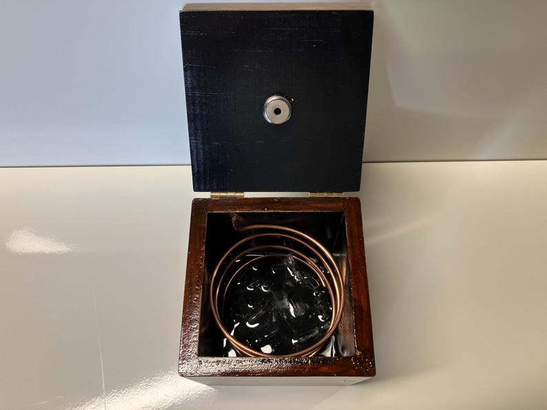 May include: A wooden box with a black interior and a copper coil inside. The box is open and the coil is visible.