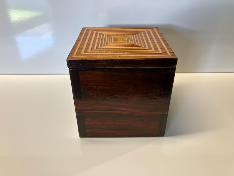 May include: A wooden box with a geometric pattern on the lid. The box is made of dark wood with a light wood inlay.