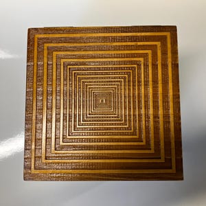 May include: A wooden box with a decorative design of concentric squares, creating an optical illusion of depth.