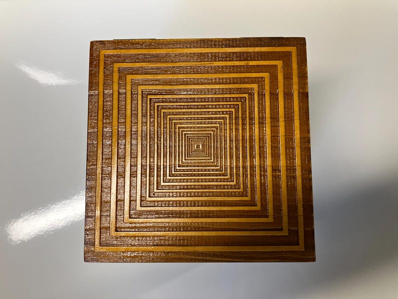 May include: A wooden box with a decorative design of concentric squares, creating an optical illusion of depth.