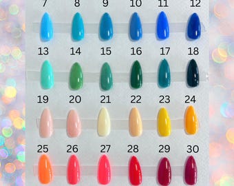 May include: A color chart featuring thirty-six almond-shaped artificial nail samples arranged in six rows of six, numbered 1 through 36. The display showcases a wide spectrum of glossy solid colors, ranging from soft pastels to vibrant neons and deep dark tones.