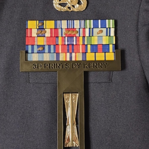 May include: A gold metal display stand with a black base and a gold metal rocket design. The stand holds a collection of military ribbons and a gold metal wreath.