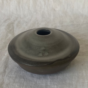 Może przedstawiać: Czarny ceramiczny wazon z szerokim, płytkim otworem i zaokrągloną podstawą. Wazon ma gładkie, matowe wykończenie.