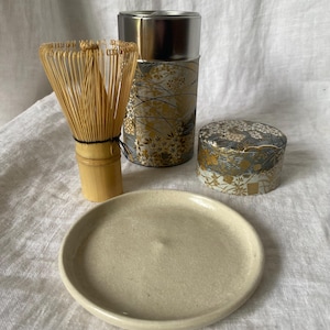 以下が含まれることがあります： 竹製の抹茶用泡立て器、小さなセラミックプレート、金と銀の花柄の装飾容器2つを備えた抹茶ティーセット。 ティーコンテナにはシルバーの蓋が付いています。