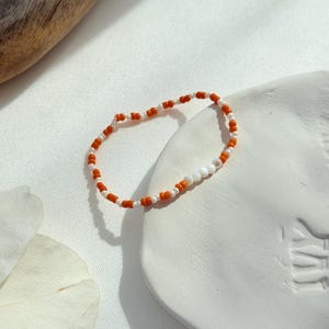Bracelet fait main en perles orange, blanches et coquillage, idéal au quotidien.