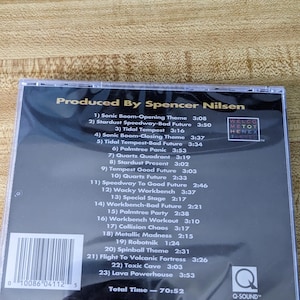 May include: A compact disc case featuring the album "Sonic CD" produced by Spencer Nilsen. The cover displays a tracklist with song titles like "Stardust Speedway" and "Palmtree Panic". The disc has a total runtime of 70:52.