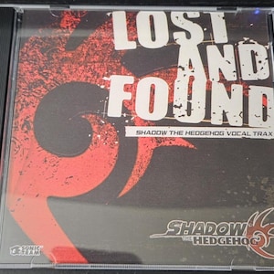 May include: A clear plastic CD jewel case featuring the album Lost and Found Shadow the Hedgehog Vocal Trax. The cover art displays a large red stylized flame graphic on a black background with white text and the Sonic Team logo in the corner.