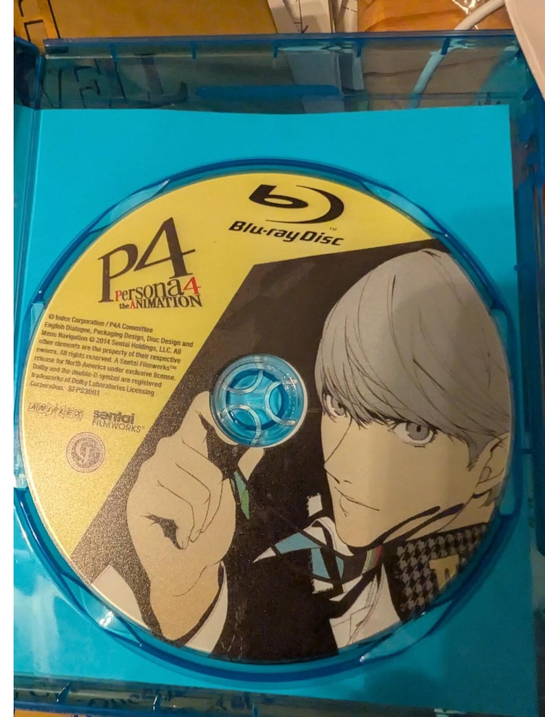 May include: A Blu-ray disc for Persona 4 The Animation housed in a blue plastic case. The disc features a yellow and black graphic of an anime character with light hair, the P4 Persona 4 The Animation logo, and the Sentai Filmworks company logo.