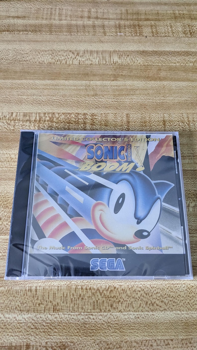 May include: A Limited Collector's Edition CD case for Sonic Boom. The cover features Sonic the Hedgehog in a dynamic pose with the text "SONIC BOOM" and "The Music From Sonic CD and Sonic Spinball" and the SEGA logo.