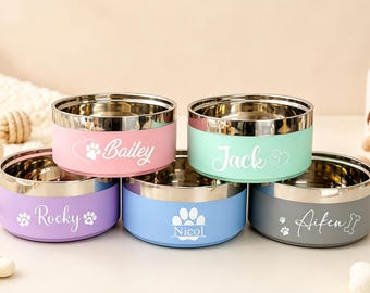 May include: Five round stainless steel pet bowls with colored exterior coatings in pink, mint green, purple, light blue, and dark gray. Each bowl features a white custom name engraving, including Bailey, Jack, Rocky, Nicol, and Aifen, with paw prints.