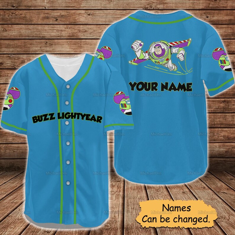 May include: A light blue baseball jersey featuring Buzz Lightyear graphics. The front displays "BUZZ LIGHTYEAR" in black, while the back has a Buzz Lightyear image and the text "YOUR NAME". Green accents trim the collar, sleeves, and button line. The jersey is a fun, themed apparel item.