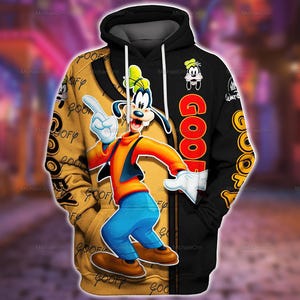 Könnte beinhalten: Ein schwarz-goldener Kapuzenpullover mit einer großen Grafik der Zeichentrickfigur Goofy, die nach oben zeigt. Das Design enthält den Schriftzug GOOFY in großen roten Buchstaben, ein kleines Goofy-Gesichtssymbol und wiederholten Text auf dem Gold.