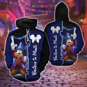 Puede incluir: Una sudadera con capucha negra y azul que presenta un gráfico de Mickey Mouse como aprendiz de brujo con un sombrero azul y una túnica roja. El diseño incluye el texto "Believe in Magic" y una silueta blanca de un castillo en forma de cabeza.
