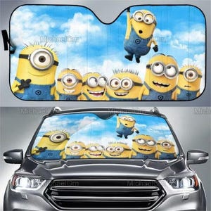 Könnte beinhalten: Ein Autosonnenschutz mit einem blauen Himmel als Hintergrund und Cartoon-Minions. Die Minions sind gelb mit blauen Overalls und Brillen. Geeignet für die Windschutzscheibe eines Autos.