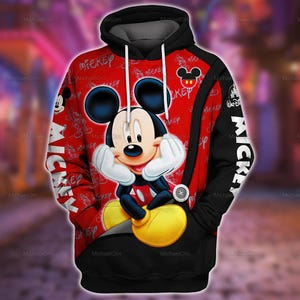 Puede incluir: Una sudadera con capucha roja y negra que presenta un gran gráfico de Mickey Mouse con guantes blancos y zapatos amarillos. La tela muestra un patrón repetido de Mickey, el texto MICKEY en blanco y un logotipo de Walt Disney en la manga negra.