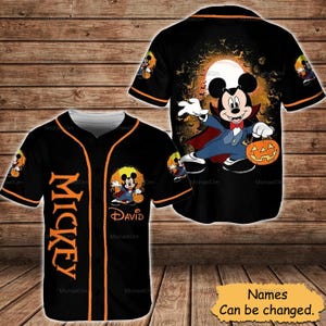May include: Black baseball jersey with orange trim and the name "MICKEY" vertically down the front. The jersey features a Halloween-themed Mickey Mouse design on the front and back, with the name "DAVID" below the character.