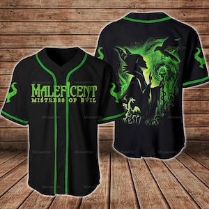 Puede incluir: Camiseta de béisbol negra con detalles verdes y el texto "MALEFICENT MISTRESS OF EVIL" en verde. La parte trasera presenta un gráfico verde y negro de Maléfica con un cuervo y un bastón. La camiseta tiene una parte delantera abotonada y detalles verdes.