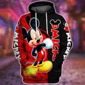 Puede incluir: Una sudadera con capucha negra y roja que presenta un gran gráfico de Mickey Mouse en la parte delantera. El diseño incluye el texto Mickey Mouse en un patrón repetitivo en el lado rojo y el nombre Mickey impreso verticalmente en blanco en el lado negro.