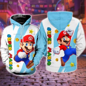May include: A white and light blue hooded sweatshirt featuring a graphic print of the character Mario from Super Mario. The design includes the text Super Mario in a vertical yellow and green font, along with gold coins and yellow stars.