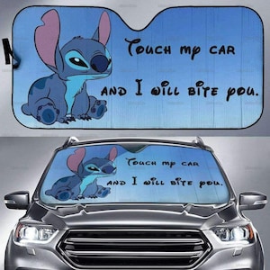 Può includere: Parasole blu per auto con un personaggio dei cartoni animati e la scritta "Touch my car and I will bite you." Il parasole è mostrato sul parabrezza di un'auto.