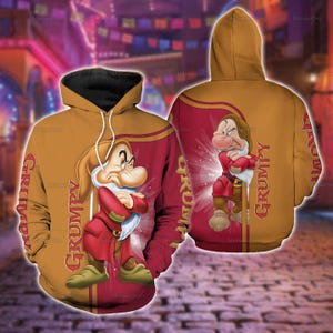 Puede incluir: Una sudadera con capucha de color amarillo mostaza y granate que presenta un gráfico del personaje Gruñón de Blancanieves con los brazos cruzados. La palabra GRUMPY está impresa verticalmente en una fuente estilizada en el frente y la espalda.