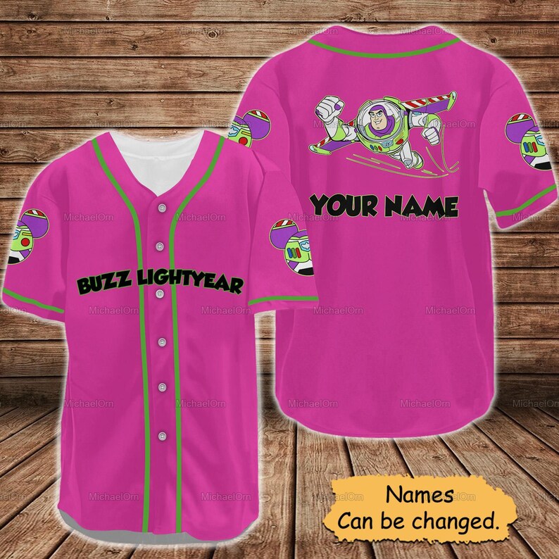 May include: A pink Buzz Lightyear baseball jersey with green trim and the text "BUZZ LIGHTYEAR" on the front. The back features a Buzz Lightyear graphic and the text "YOUR NAME". The sleeves have a Buzz Lightyear graphic.