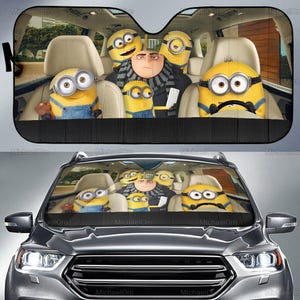 Puede incluir: Parasol de coche con una imagen colorida de Gru y los Minions dentro de un coche. El parasol es negro con una textura de malla. Los Minions son amarillos con monos azules.