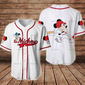 Puede incluir: Camiseta de b&eacute;isbol blanca con ribete rojo y la palabra "Mickey" en escritura roja. La camiseta presenta im&aacute;genes de dibujos animados de Mickey Mouse jugando al b&eacute;isbol. La parte posterior de la camiseta tambi&eacute;n tiene un gr&aacute;fico de b&eacute;isbol de Mickey Mouse.