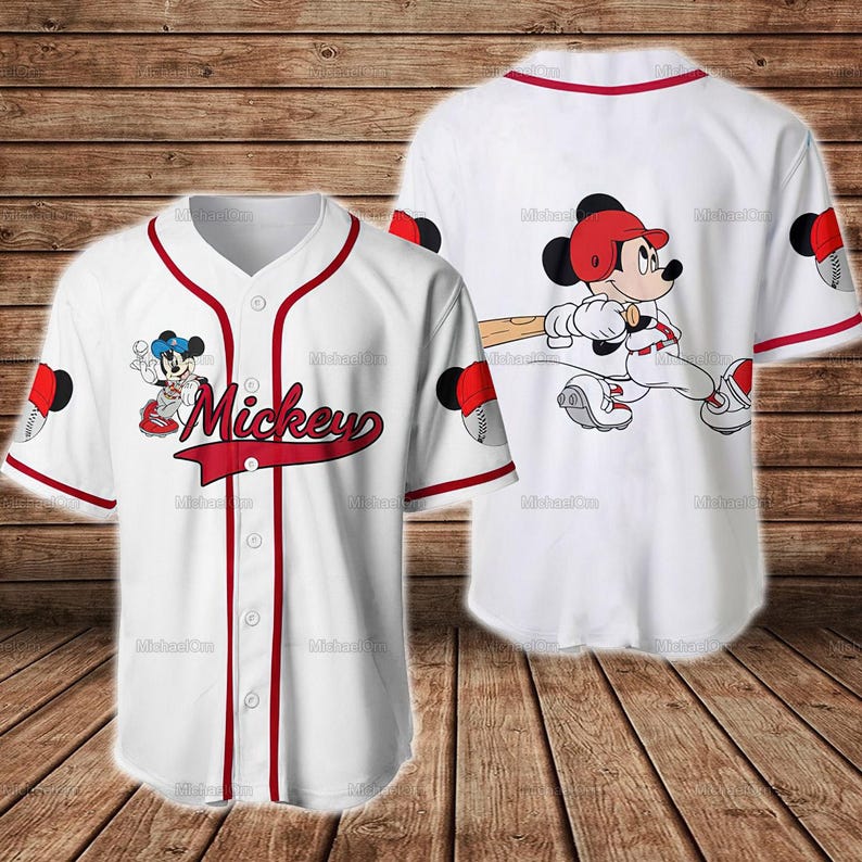 Puede incluir: Camiseta de b&eacute;isbol blanca con ribete rojo y la palabra "Mickey" en escritura roja. La camiseta presenta im&aacute;genes de dibujos animados de Mickey Mouse jugando al b&eacute;isbol. La parte posterior de la camiseta tambi&eacute;n tiene un gr&aacute;fico de b&eacute;isbol de Mickey Mouse.